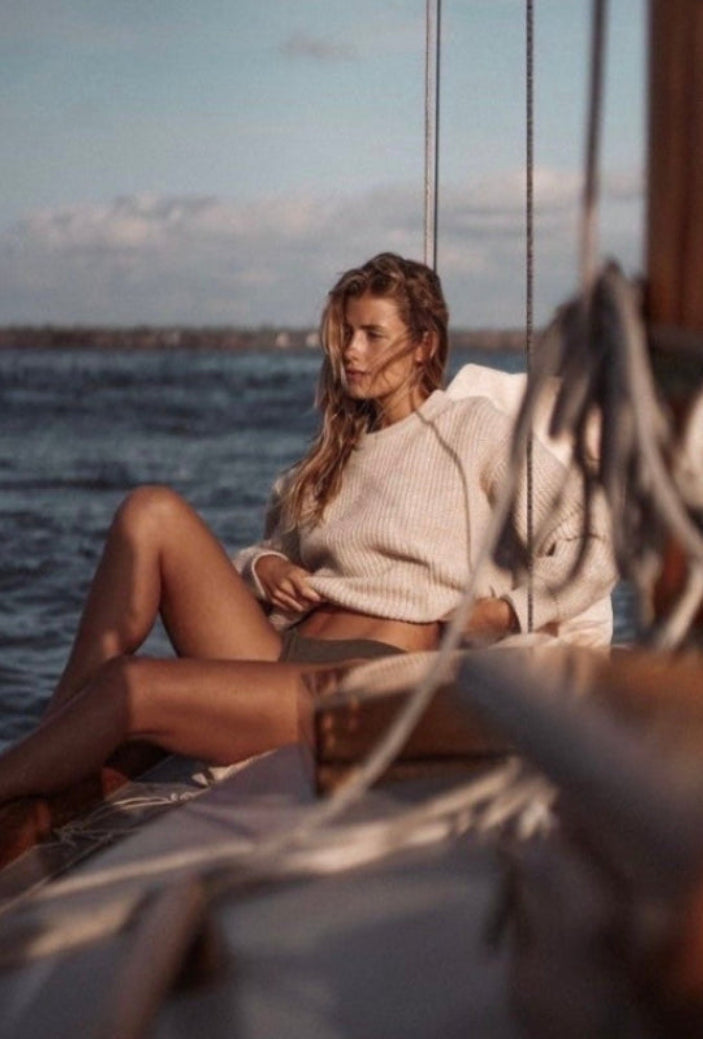 Woman sitting on a sailboat with water and sky in the background